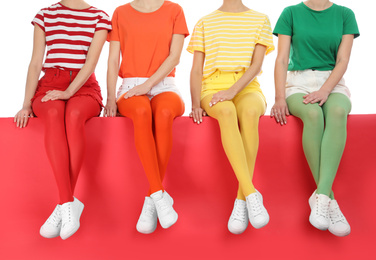 Women wearing bright tights sitting together on color background, closeup