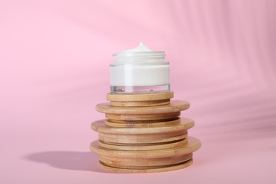 Photo of Open jar of cream on wooden display against pink background