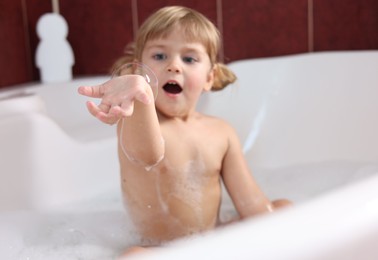 Photo of Little girl showing bubble in bathtub at home, selective focus