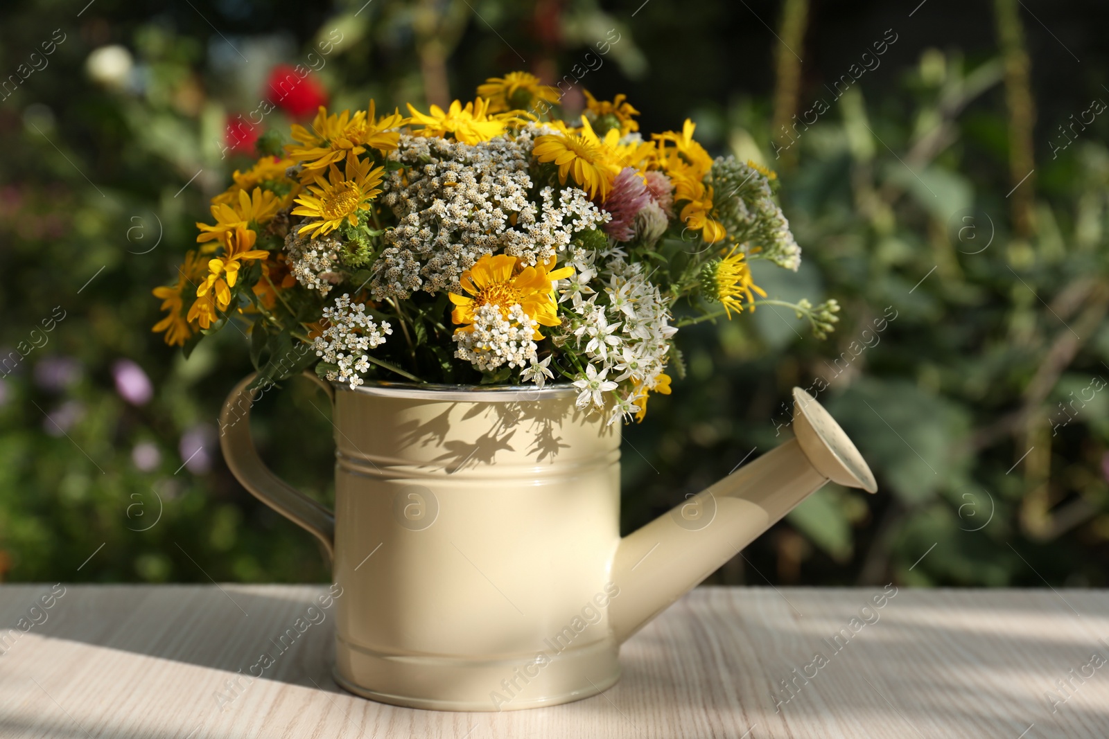 Photo of Beautiful bouquet of bright wildflowers in watering can on white wooden table outdoors