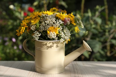 Beautiful bouquet of bright wildflowers in watering can on white wooden table outdoors