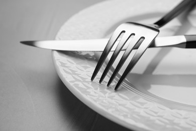 Photo of Plate with fork and knife on grey table, closeup