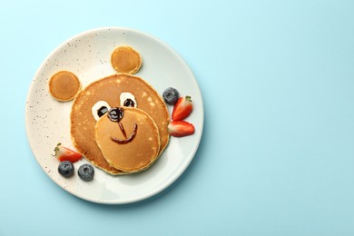 Photo of Creative serving for kids. Plate with cute bear made of pancakes and berries on light blue table, top view. Space for text