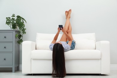 Young woman using smartphone on sofa at home. Internet shopping