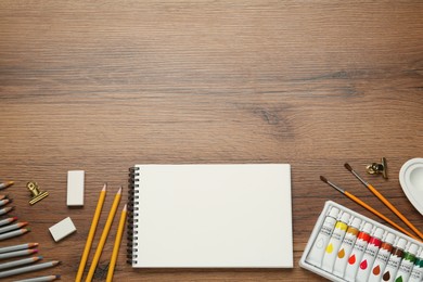 Flat lay composition with sketchbook and drawing tools on wooden table, space for text