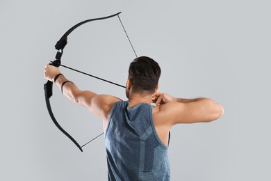 Photo of Man with bow and arrow practicing archery on light grey background, back view