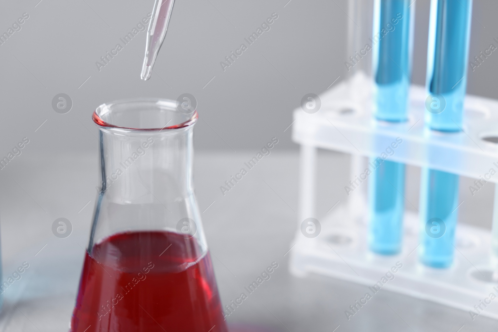 Photo of Dripping liquid from pipette into flask on grey background, closeup