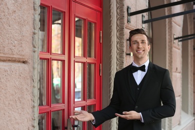 Photo of Young doorman in elegant suit standing near restaurant entrance