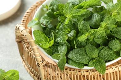 Photo of Wicker tray with bowl of fresh green mint leaves on grey table, closeup