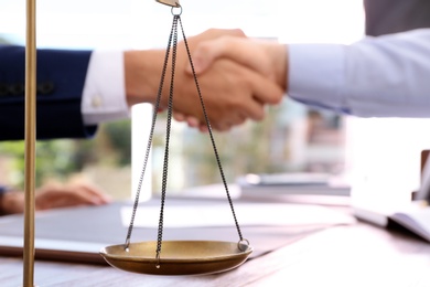 Photo of Scales of justice and blurred lawyer handshaking with client on background