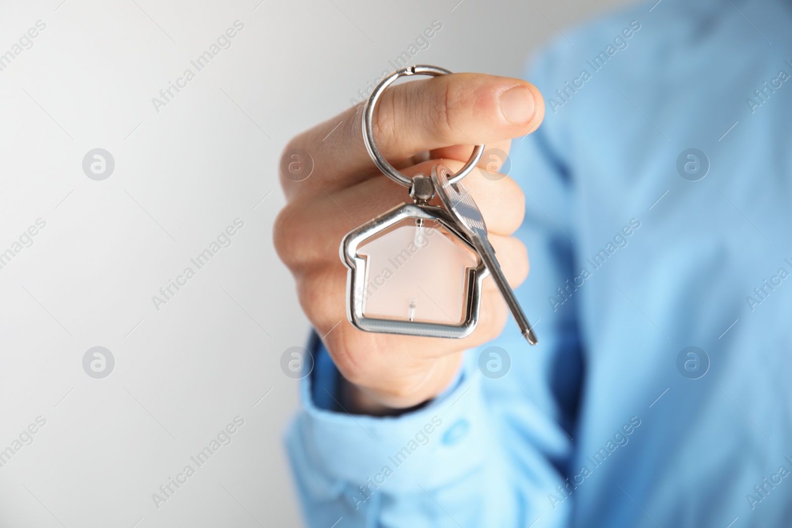 Photo of Man holding house key with trinket on light background, closeup. Space for text