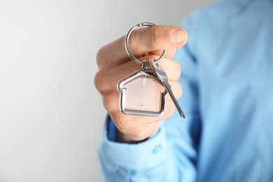 Man holding house key with trinket on light background, closeup. Space for text