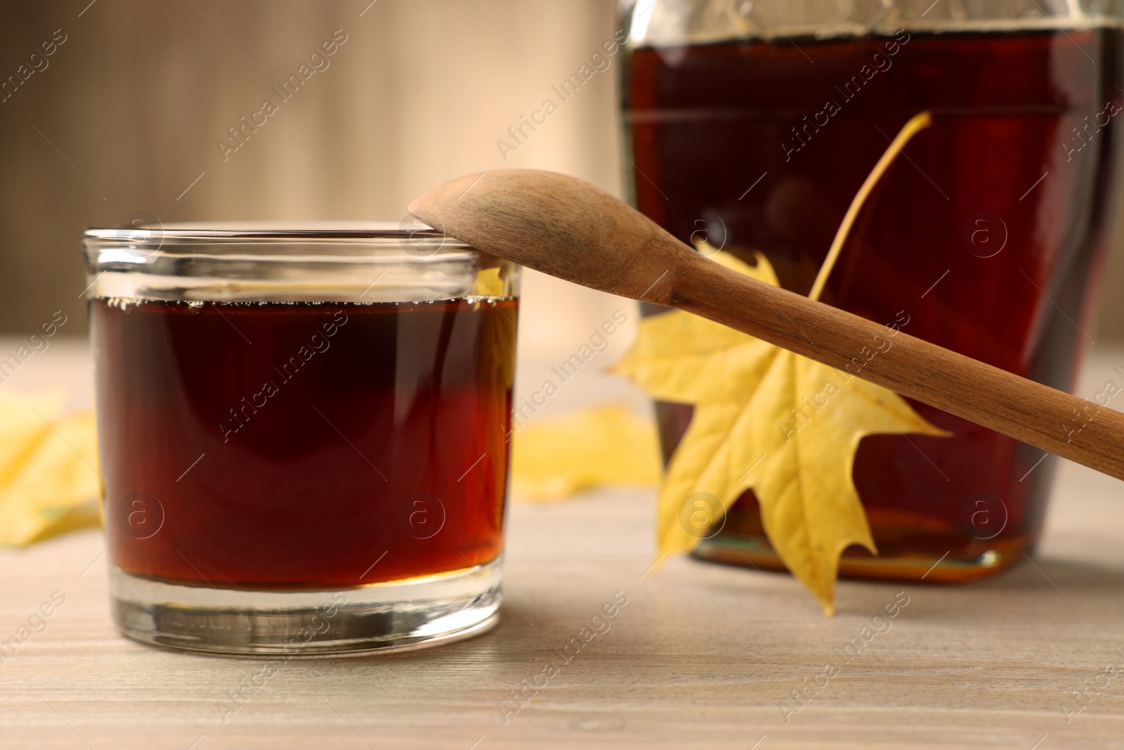 Photo of Tasty maple syrup, spoon and leaves on wooden table, closeup