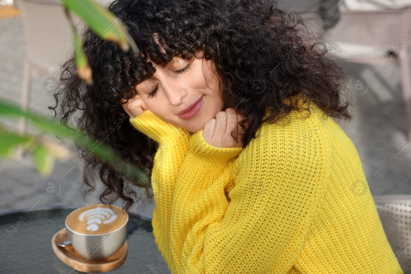 Photo of Young woman in stylish yellow sweater with cup of coffee at table outdoors