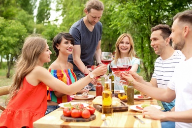 Photo of Young people with glasses of wine at table outdoors. Summer barbecue