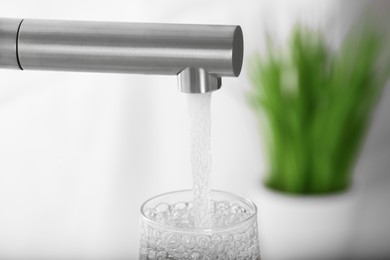Photo of Filling glass with tap water from faucet on blurred background, closeup