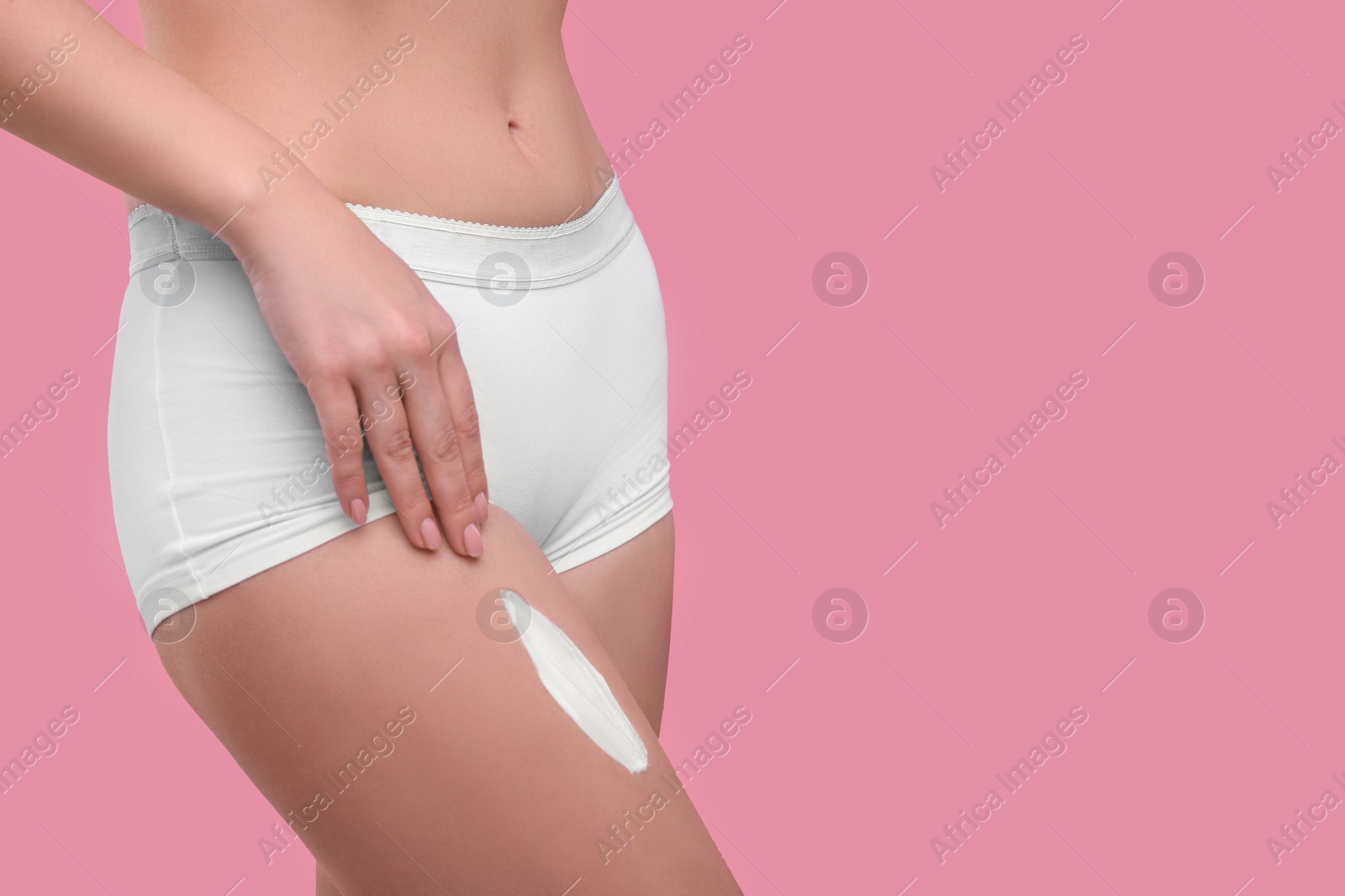 Photo of Woman with smear of body cream on her leg against pink background, closeup. Space for text
