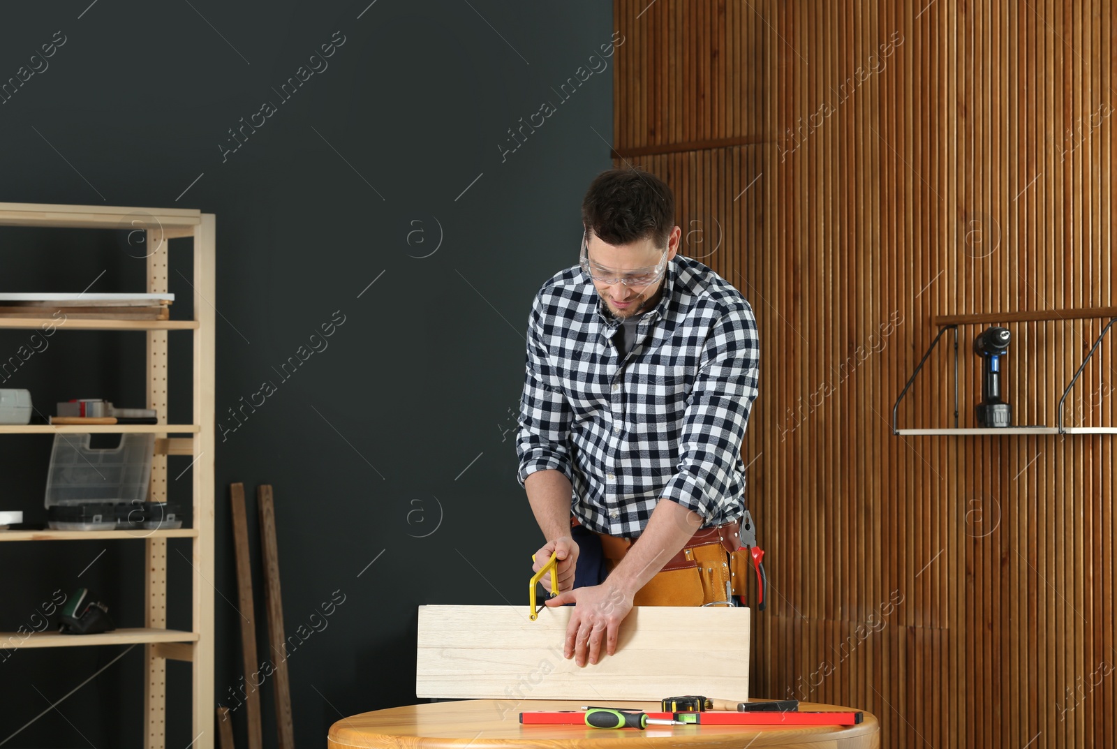 Photo of Handsome working man using hand saw indoors. Home repair