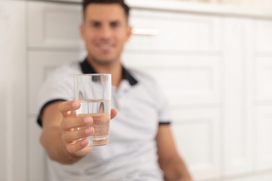 Photo of Man holding glass of pure water in kitchen, focus on hand. Space for text