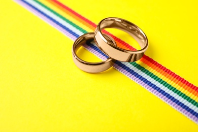 Photo of Wedding rings and rainbow ribbon on color background. Gay symbol