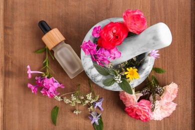 Photo of Bottle of essential oil, marble mortar and different flowers on wooden board, top view