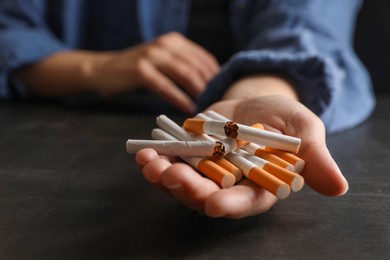 Stop smoking. Woman holding whole and broken cigarettes at black table, closeup