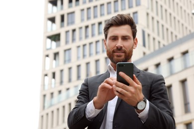 Photo of Handsome businessman with smartphone near buildings, space for text