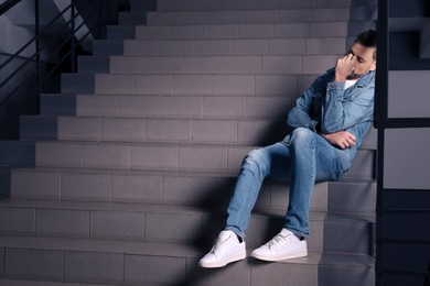 Upset man sitting on stairs indoors, space for text. Loneliness concept