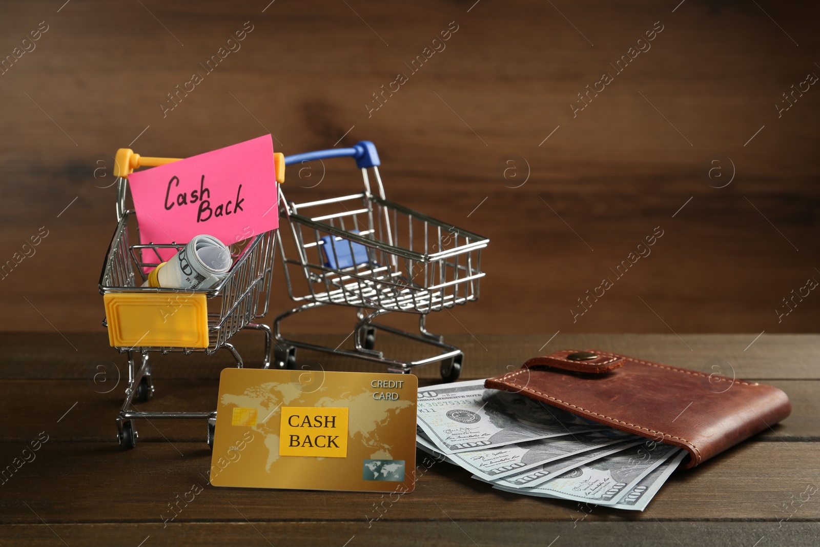 Photo of Composition with signs Cash Back, credit card and small shopping carts on wooden table