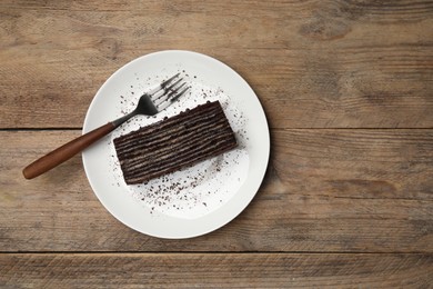 Photo of Plate with tasty Spartak cake and fork on wooden table, top view. Space for text