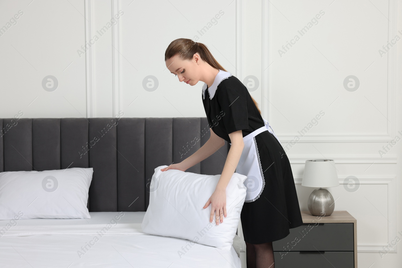 Photo of Young maid making bed in hotel room