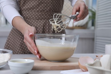 Woman making dough with whisk in bowl at table, closeup