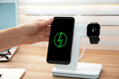 Photo of Woman putting mobile phone onto wireless charger at wooden table, closeup. Modern workplace accessory