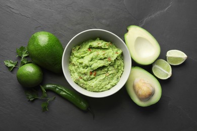 Photo of Delicious guacamole, fresh avocado and parsley on dark grey table, flat lay
