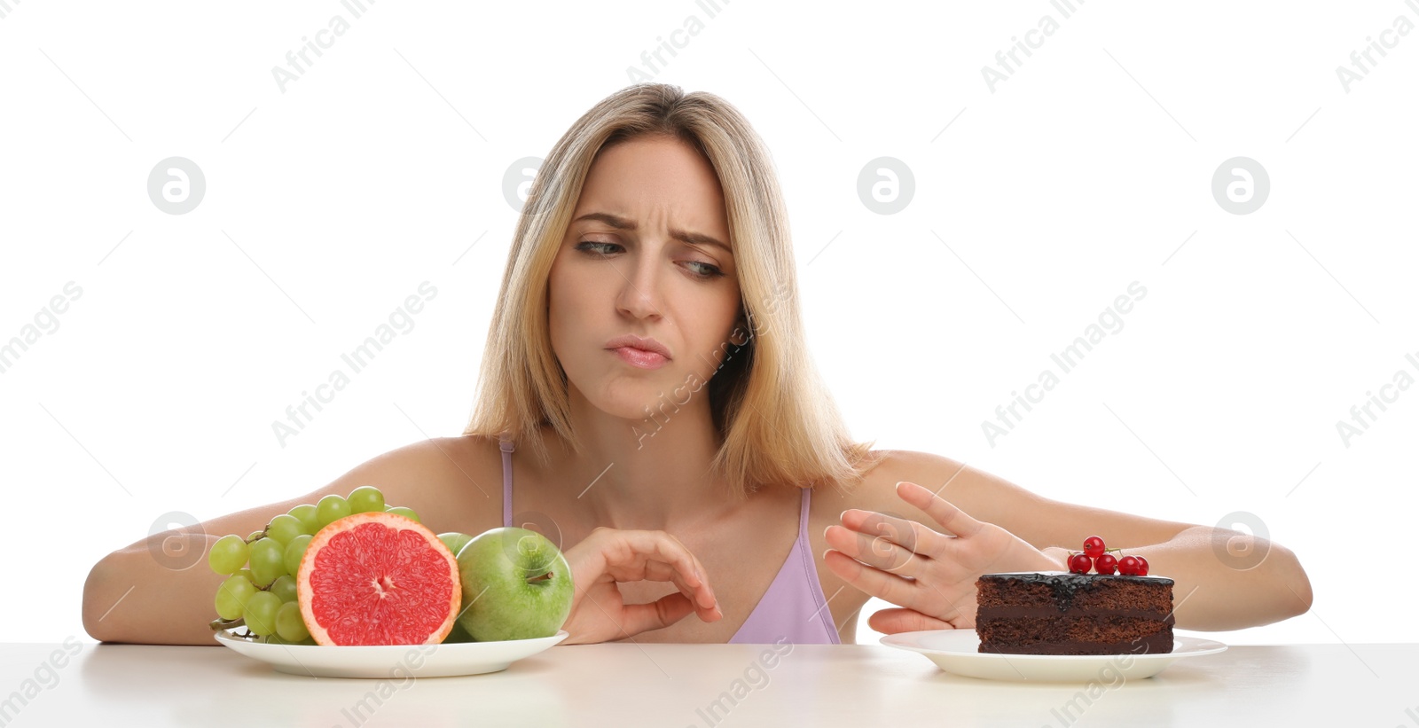 Photo of Woman choosing between cake and healthy fruits at table on white background