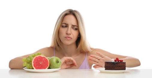 Photo of Woman choosing between cake and healthy fruits at table on white background