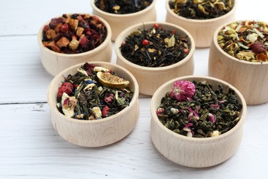 Photo of Different kinds of dry herbal tea in bowls on white wooden table