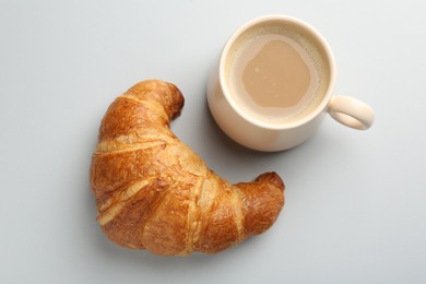 Delicious fresh croissant and cup of coffee on light background, flat lay