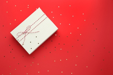 Photo of Gift box and confetti stars on red background, flat lay. Christmas celebration