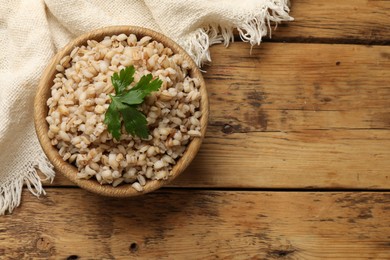 Photo of Delicious pearl barley with parsley in bowl on wooden table, top view. Space for text