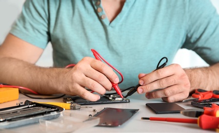 Photo of Technician checking mobile phone at table in repair shop, closeup