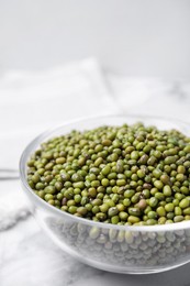 Photo of Glass bowl with green mung beans on white marble table, closeup