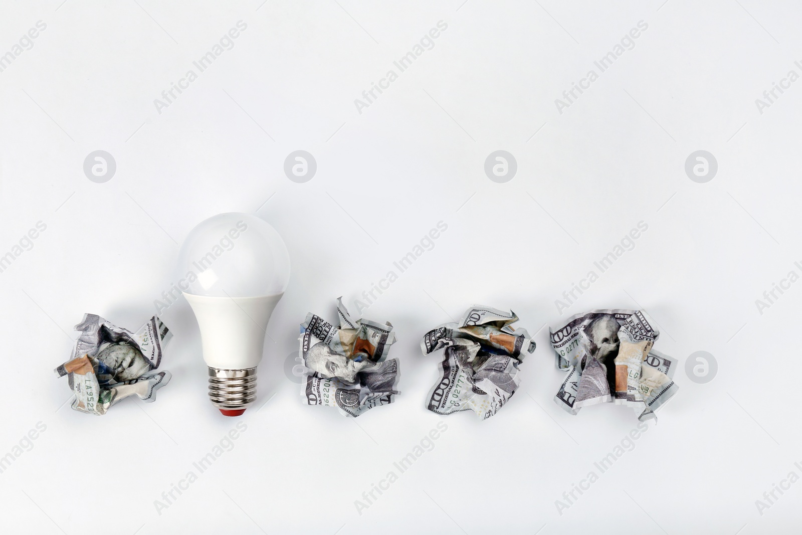 Photo of Composition with lamp bulb, crumpled banknotes and space for text on white background, top view. Creative concept