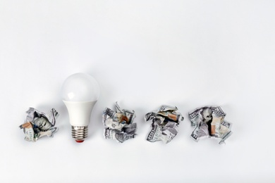 Photo of Composition with lamp bulb, crumpled banknotes and space for text on white background, top view. Creative concept