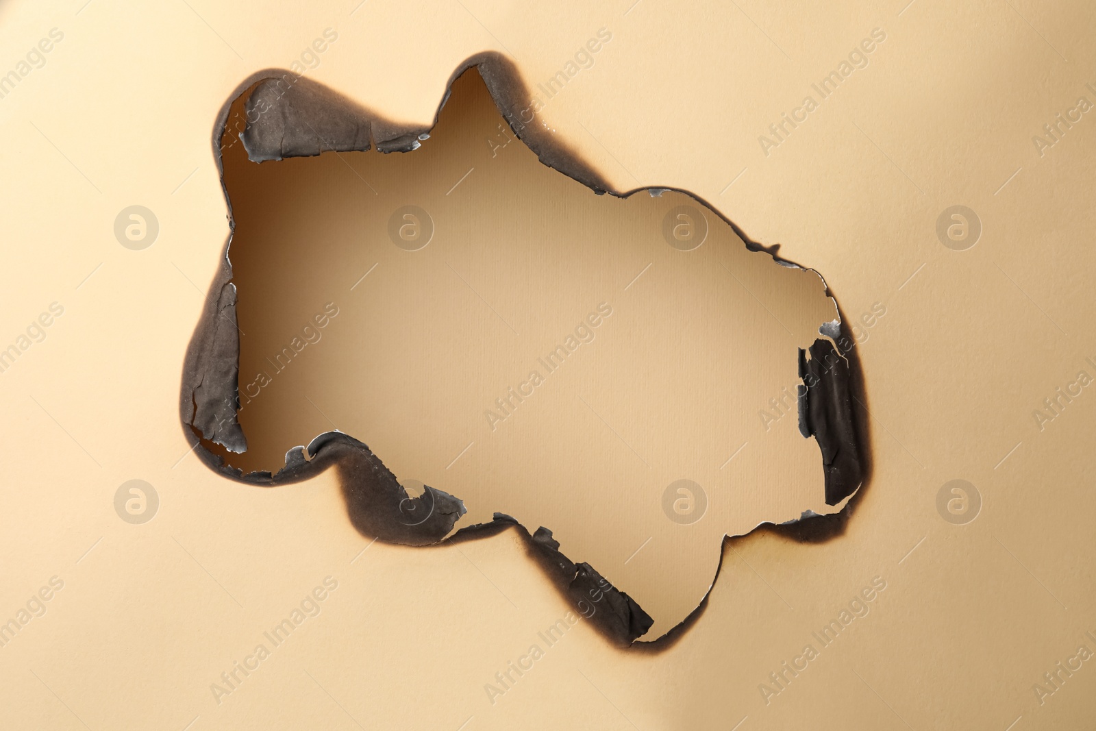 Photo of Burnt hole in paper on beige background, space for text