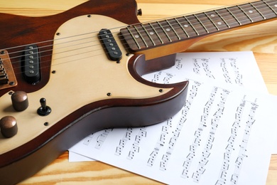 Modern electric guitar and music sheets on wooden background