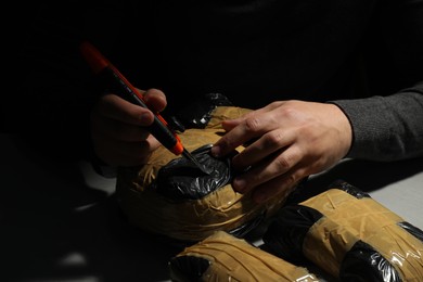 Photo of Smuggling and drug trafficking. Man opening package of narcotics with box cutter in darkness, closeup