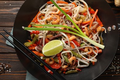 Photo of Shrimp stir fry with noodles and vegetables in wok on wooden table, top view