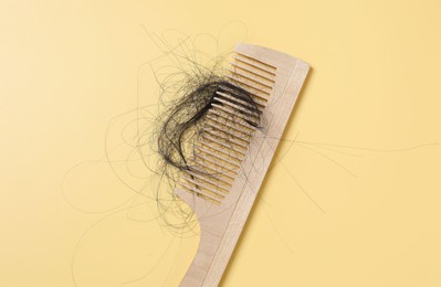 Photo of Wooden comb with lost hair on yellow background, top view