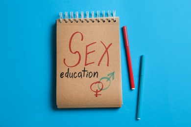 Photo of Notebook with phrase "SEX EDUCATION" and gender symbols on blue background, flat lay